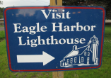 blue directional sign with Visit Eagle Harbor Lighthouse written on it